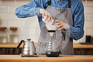 Closeup of male barista pouring ground coffee making pourover.