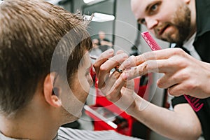 Closeup.Male hairdresser cuts young client with scissors with serious face, focus on hands.Professional male hairdresser creates a