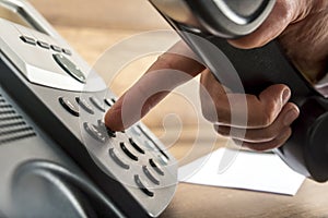 Closeup of male hand dialing a telephone number on black landlin