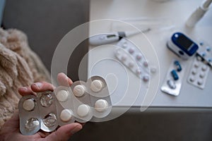 Closeup male hand holding medicament and first aid kit top view. drug, pill and thermometer on table