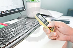 Closeup male hand holding old-fashioned push-button mobile phone sitting at white desktop. Staying at home, working remotely,