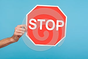 Closeup of male hand holding Stop symbol, showing red traffic sign, warning about problems, concept of ban