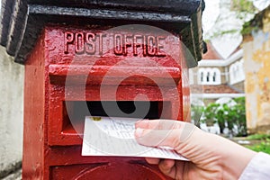 Closeup on a male hand putting a letter in a red letterbox. Concept of vintage type of communication.