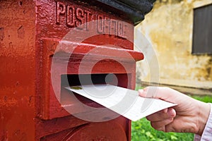 Closeup on a male hand putting a letter in a red letterbox. Concept of vintage type of communication.