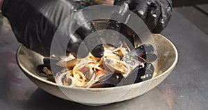 Closeup male hands of chef or food stylist serving italian seafood pasta laying out mussels on a plate in the kitchen