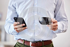 Closeup of male hands holding coffee and smartphone. Businessman using mobile phone to send text, browse social media or