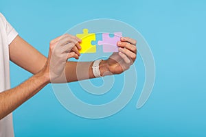 Closeup of male hands holding two puzzle parts, ready to connect colorful jigsaw pieces, symbol of unity and association