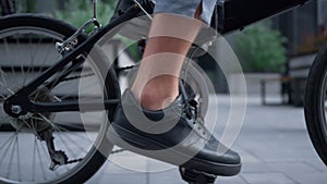 Closeup male legs pedaling city street in black shoes. Green transportation