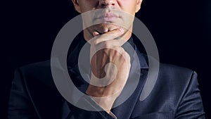 Closeup of a man in black clothes on black background. 4k. Slow motion. man strokes his chin and looks at the camera