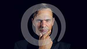 Closeup of a man in black clothes on black background. 4k. Slow motion. man strokes his chin and looks at the camera