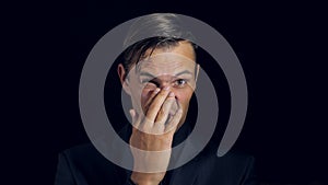 Closeup of a man in black clothes on black background. 4k. Slow motion. man strokes his nose and looks at the camera