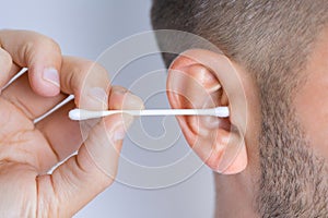 Closeup of man cleaning dirty ears with cotton swab or cotton stick. Ear cleaning and ear care