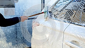 Closeup of man cleaning dirty white car with soft brush on self service car wash