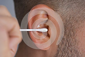 Closeup of man cleaning ear with cotton swab or cotton stick. Ear cleaning and ear care