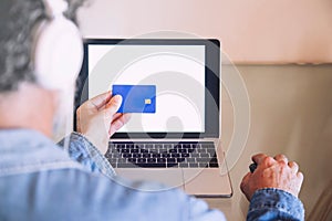 Closeup of man in front of a laptop with a blue credit card in his hand doing an online shopping