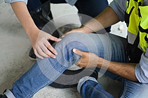 Closeup man hand in safety vest, gripped his knee with both hands. Due to injuries at the construction site