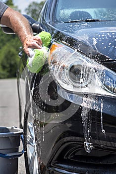Closeup man hand washing new black car with big soft sponge, soap suds and bucket