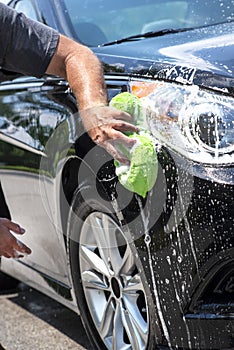 Closeup man hand washing new black car with big soft sponge, soap suds and bucket