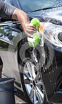 Closeup man hand washing new black car with big soft sponge, soap suds and bucket