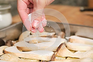 Closeup of man hands adding salt over sliced king trumpet mushrooms pleurotus eryngii, potatoes and onions