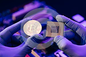 Closeup of man hands in gloves hold gold Bitcoin and cpu on motherboard background. Person shows future currency. Mining