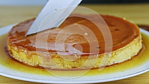 Closeup on man hands by knife cut round homemade soft flan with caramel syrup