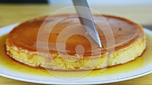 Closeup man hands by knife start to cut round soft flan with caramel syrup