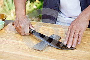 Closeup man hands sharpen knife on whetstone sharpener or grindstone.