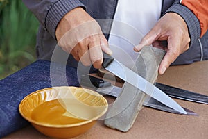 Closeup man hands sharpen knife on whetstone sharpener or grindstone.