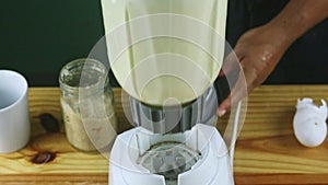 Closeup man hands take big glass chalice with mixed milk from electric blender stand