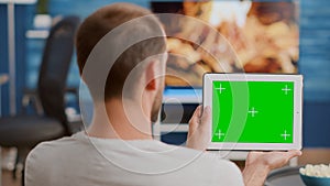 Closeup of man holding digital tablet with green screen watching webinar sitting on sofa