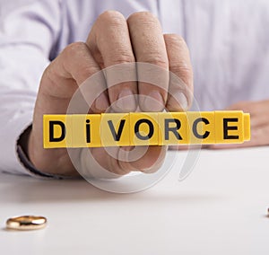 Closeup of a man holding divorce text, wedding rings