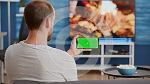 Closeup of man holding smartphone with green screen watching online video content