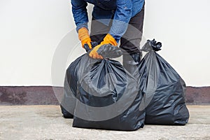 Closeup man holds black plastic bag that contains garbage inside.