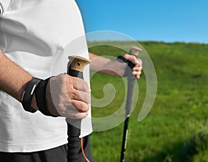 Closeup of man keeping tracking sticks on green grass background.