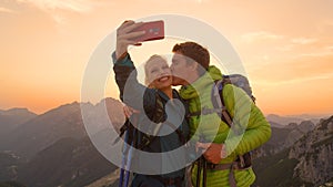 CLOSEUP: Man kisses his smiling girlfriend taking a photo of them in the Alps.