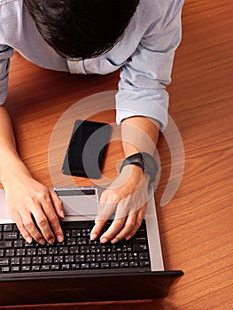 Closeup of a man laying typing on laptop wearing smart-watch and mobilephone beside.