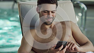 Closeup man looking phone by pool. Male relaxing with phone at wellness center