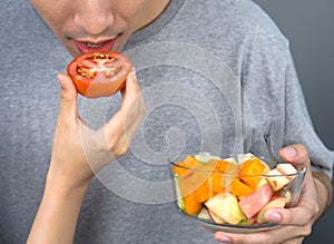 Closeup man mouth, eating a piece of tomato from woman hand while holding fruit salad bowl