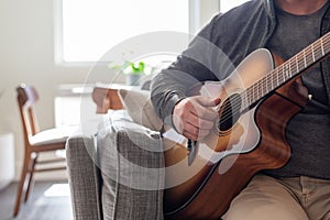 Closeup of man playing acoustic guitar at home in natural light