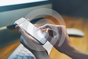 Closeup of a man pointing finger to smartphone with a blank screen monitor in the hands, working behind a computer keyboard