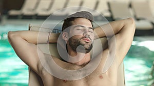 Closeup man relaxing by pool at luxury spa. Man sleeping poolside on lounger