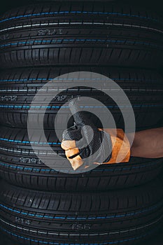 Closeup man's gloved hand, raising his thumb top against background car tires. Concept of car service.