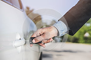 Closeup of a man`s hand inserting a key into the door lock of a car. Horizontal format. Car and man are unrecognizable