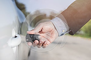 Closeup of a man`s hand inserting a key into the door lock of a car. Horizontal format. Car and man are unrecognizable