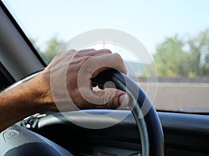 Closeup of a man's hand navigating the steering wheel inside a car in a sunny city
