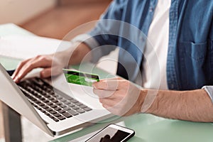 Closeup of man`s hands holding bank credit card and using laptop