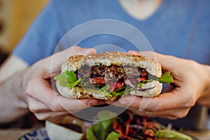 Closeup of man`s hands holding vegan chickpea and bean burger with fresh greens