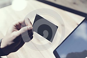 Closeup Man Showing Blank Black Business Card, Holding Hand Modern Digital Tablet.Wood table Blurred Background.Mockup