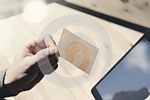 Closeup Man Showing Blank Craft Business Card, Holding Hand Modern Digital Tablet.Wood table Blurred Background.Mockup